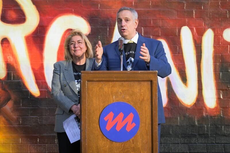 man speaking behind a podium and woman standing next to him