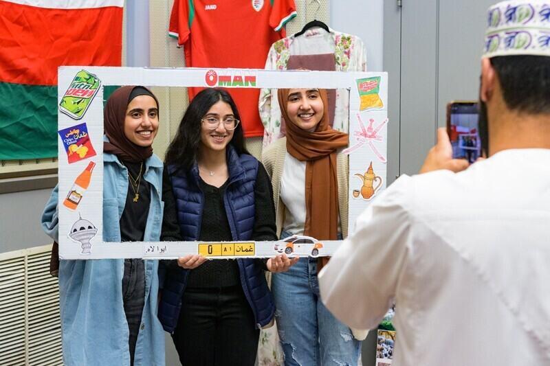three people standing with a cut-out sign reading "Oman"