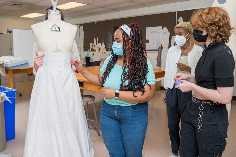 people looking at a white gown on a dress form