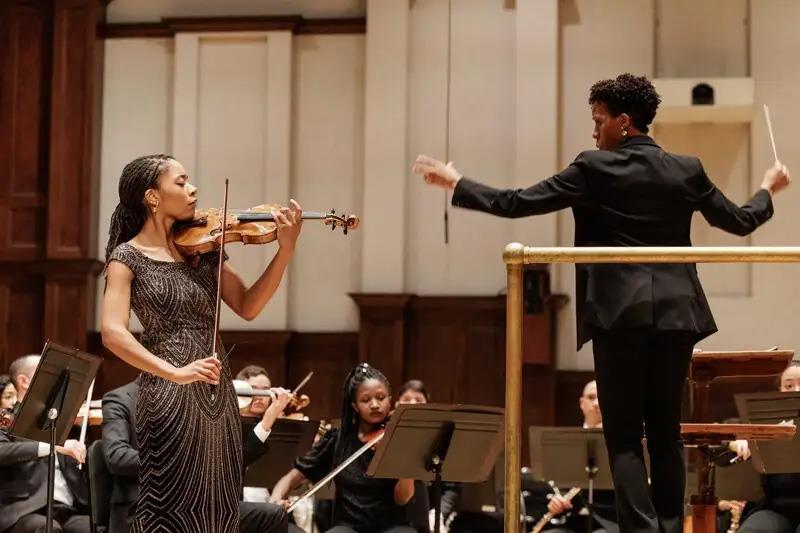 Njioma Grevious plays the violin to the left of a conductor