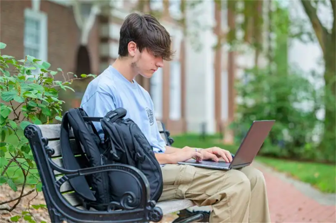 A picture of a student on a bench using his laptop