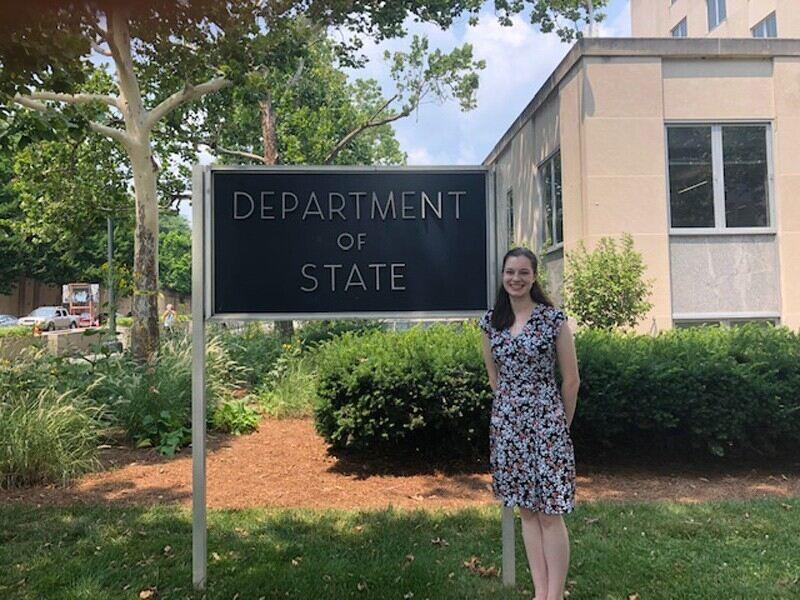 woman standing by sign saying "department of state"