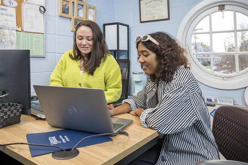 University of Delaware Student Success Center advisor (woman in yellow sweater) meets with female college student, working on laptop inside an office.