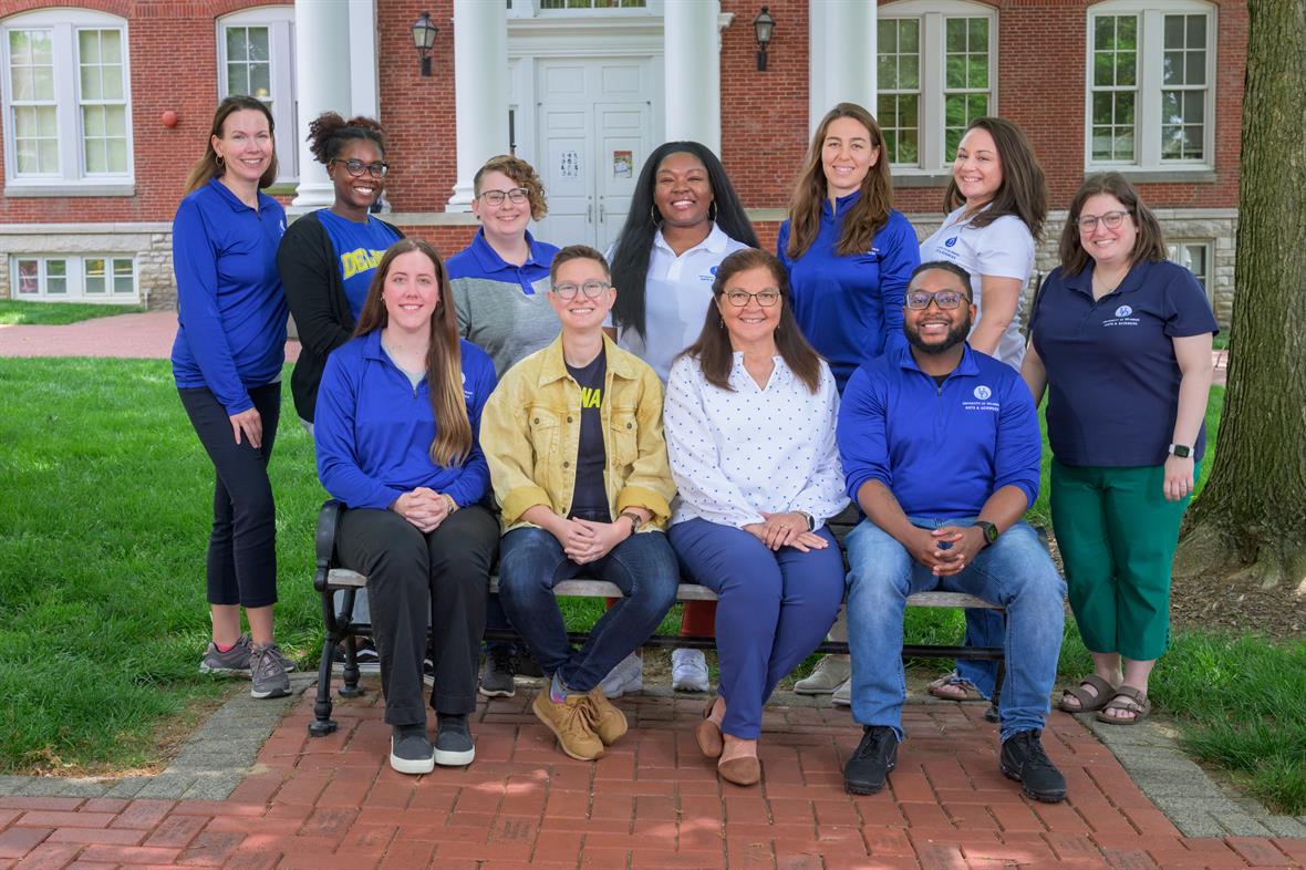 Student Success Center team, dressed in UD colors, sitting on a bench on the university's campus.